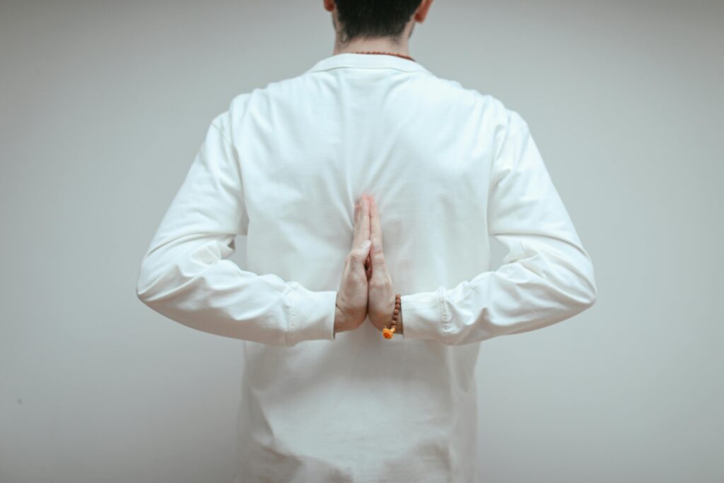 Back view of adult meditating in yoga pose with hands in reverse prayer position, embracing tranquility.